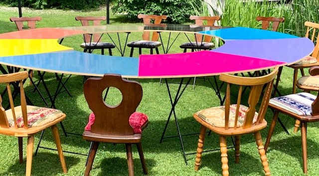 Der Runde Tisch im Garten — eine bunte runde Tafel mit Stühlen auf der Wiese